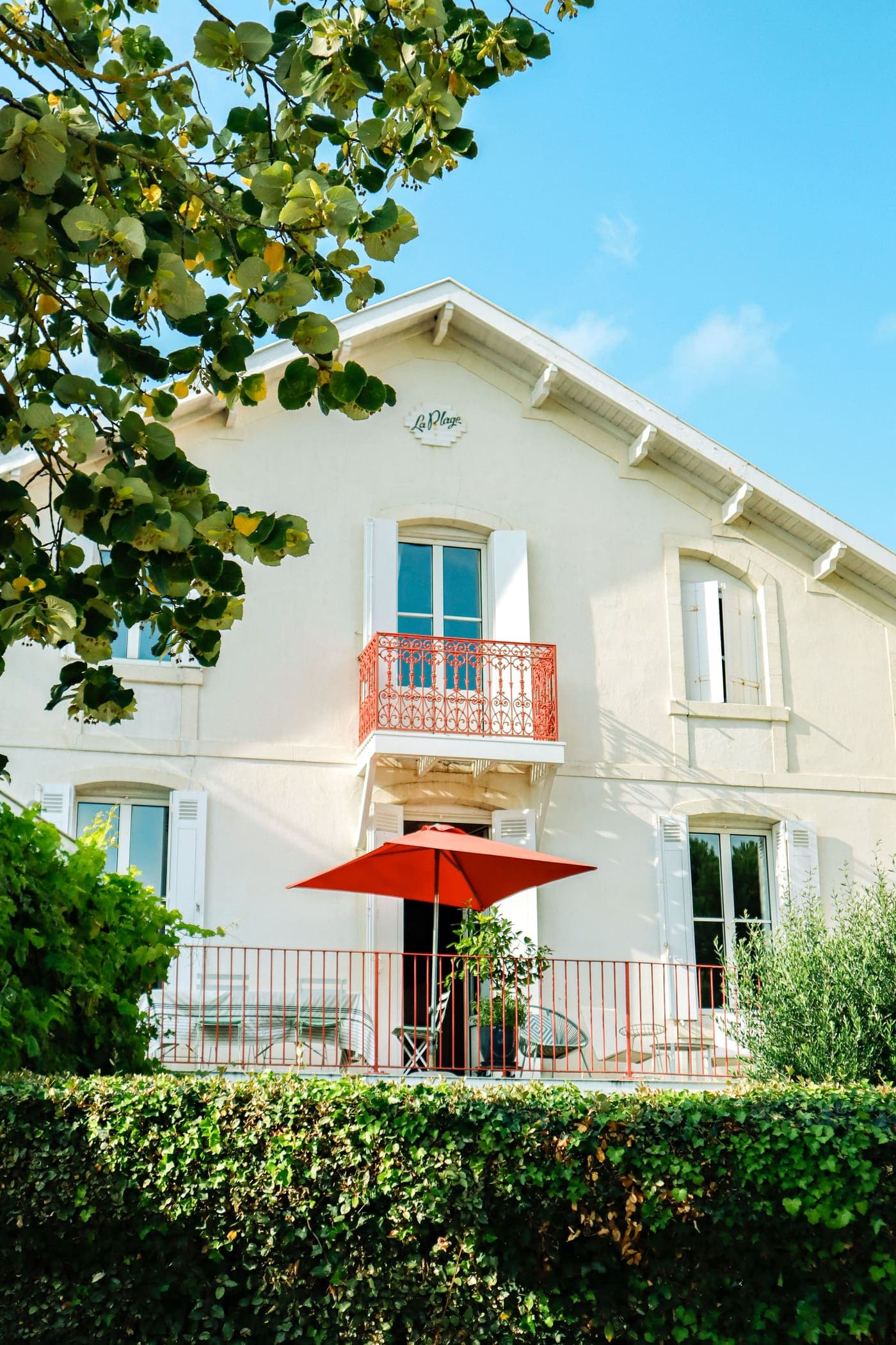 A cream house with a red parasol and a garden hedge
